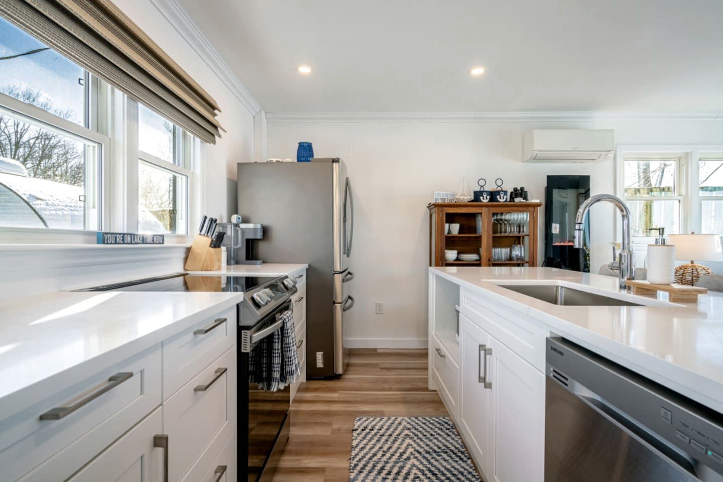 Cocina moderna con horno empotrado, refrigerador, lavavajillas, armarios de madera y un ventanal grande.