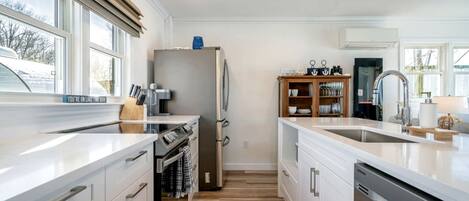 Cocina moderna con horno empotrado, refrigerador, lavavajillas, armarios de madera y un ventanal grande.
