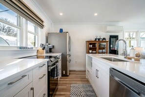 A modern kitchen with a built-in oven, refrigerator, and dishwasher, wooden cabinets, and a large window. - Stunning Cottage with Nice Views and Fire Pit in Leamington, Ontario (Leamington)