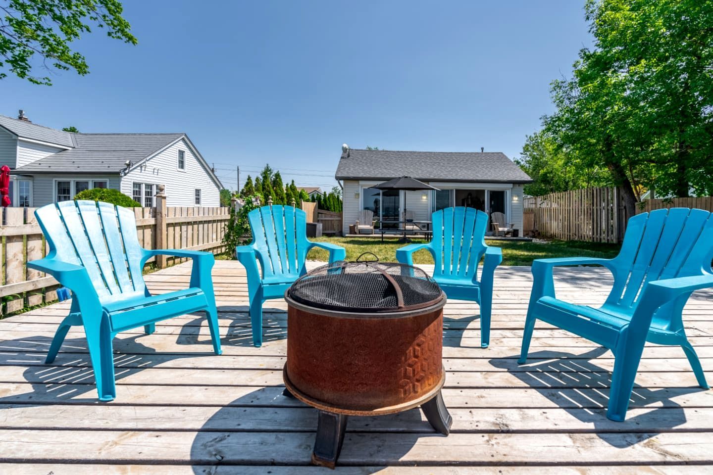 Una terraza con cuatro sillas Adirondack azules, un brasero metálico redondo y una cubierta de madera.