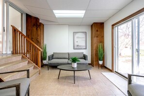 Ein modernes Wohnzimmer mit Treppe, einer Couch, einem Couchtisch und Topfpflanzen.