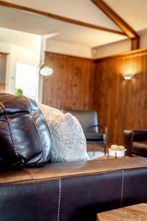 Ein ledernes Sofa mit einer strukturierten Kissen, eine Holzwand und ein Sessel in einem modern gestalteten Raum.