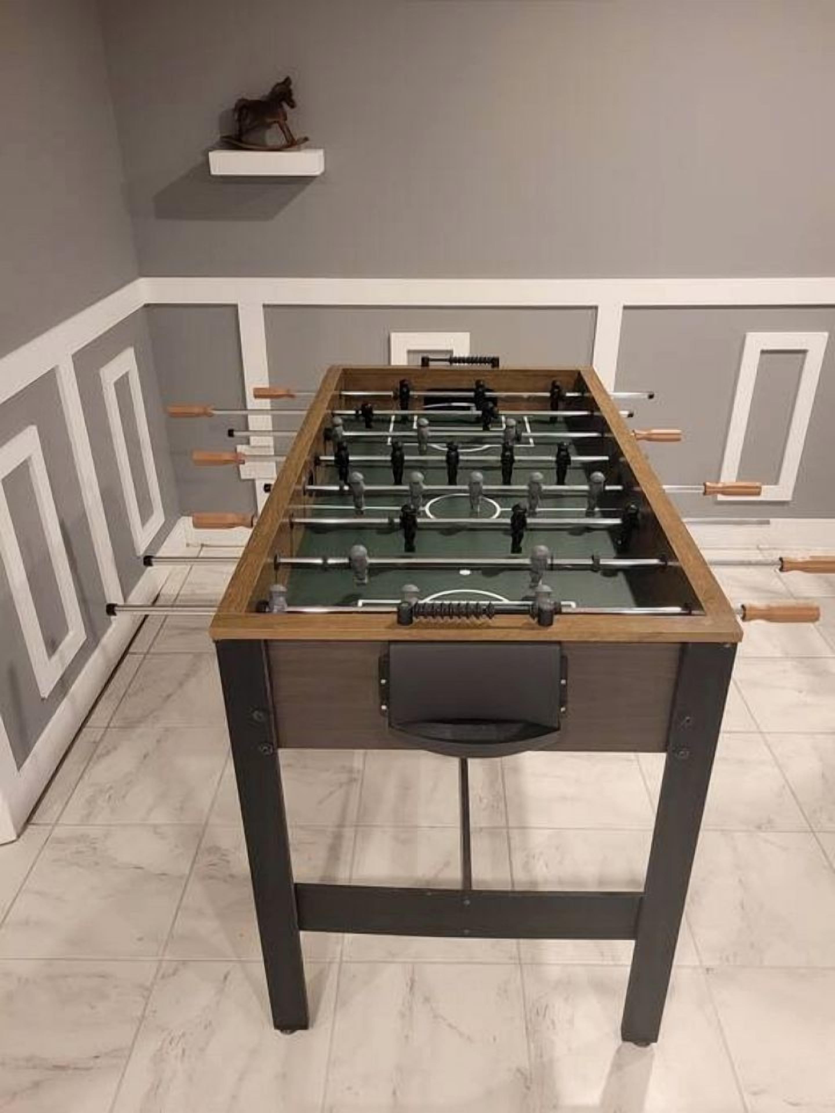 Uma mesa de futebol de mesa em um quarto com piso de azulejos e uma prateleira com uma estatueta.