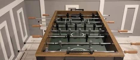 Una mesa de fútbol de mesa en una habitación con suelo de baldosas y una estantería con una figurita.