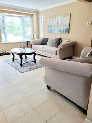 A living room with a beige sofa, a round coffee table, and a painting on the wall. - Scenic Burnt River Cottage with River Views and Outdoor Gazebo, Near Fenelon Falls and Bobcaygeon, Ontario (Kawartha Lakes)