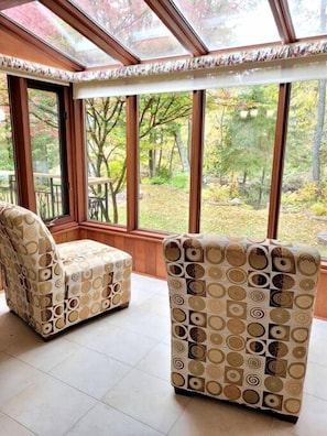 A sunroom with large windows, two patterned armchairs, and a view of a wooded area. - Scenic Burnt River Cottage with River Views and Outdoor Gazebo, Near Fenelon Falls and Bobcaygeon, Ontario (Kawartha Lakes)