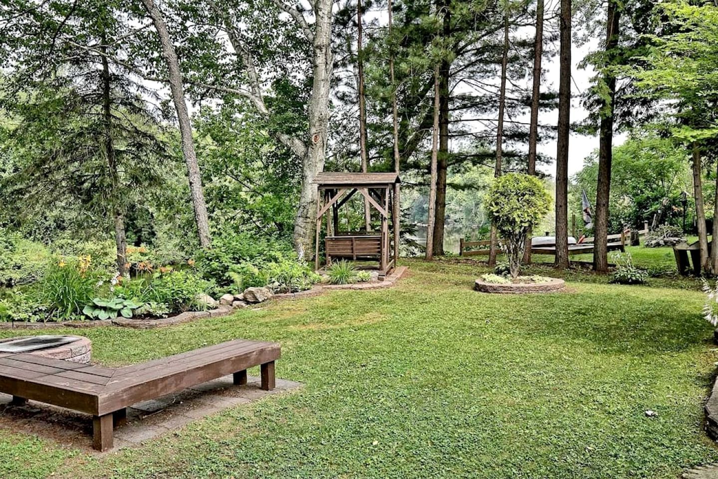 Un quiosco de madera en un jardín con un banco y un pequeño estanque.