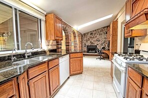 Une cuisine avec des meubles en bois, une cheminée en pierre, un lave-vaisselle et une cuisinière.