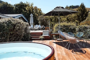 A wooden deck with a hot tub, outdoor seating, and a large umbrella.