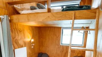 A compact, wooden interior with bunk beds, a small seating area, and a window providing natural light.