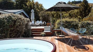 Eine Holzterrasse mit Whirlpool, Sitzgelegenheit und einem großen Sonnenschirm.