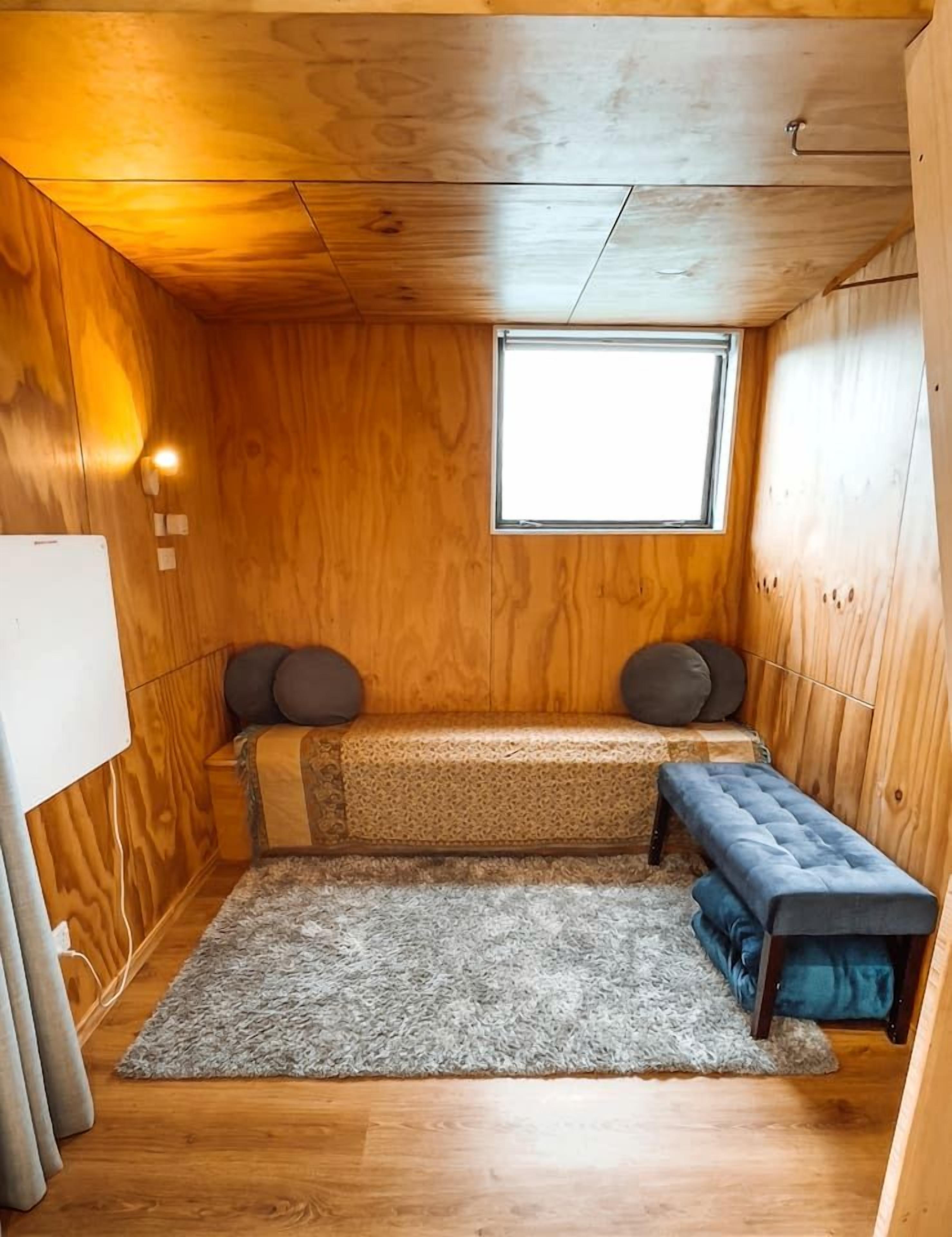 Ein kleiner Raum mit Holzwänden, einem kleinen Fenster, einer Bank und einem Teppich.
