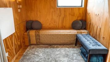 Ein kleiner Raum mit Holzwänden, einem kleinen Fenster, einer Bank und einem Teppich.