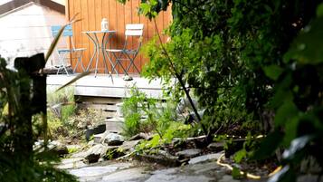 A patio with a table and chairs, surrounded by greenery and a wooden fence.