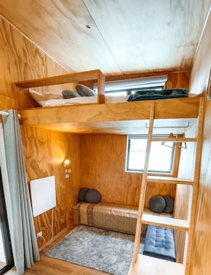 A compact, wooden interior with bunk beds, a small seating area, and a window providing natural light.