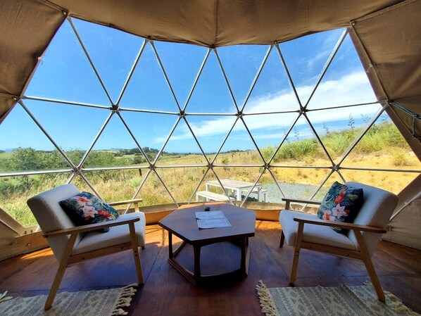 Una tienda en forma de domo geodésico con dos sillas y una mesa, ventanas amplias y vistas del paisaje.