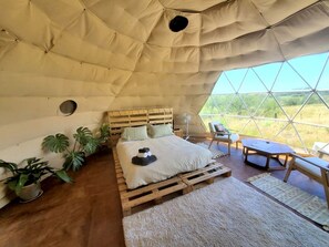Una habitación con tienda de campaña acogedora, una cama, plantas en la mesita de noche, un ventilador y vistas al exterior.