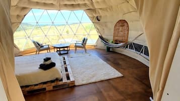 A tent with a wooden floor, a bed, a table, chairs, and a view of the landscape.