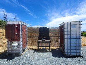 Instalación de baño portátil con estructura metálica, banca de madera y lavamanos.