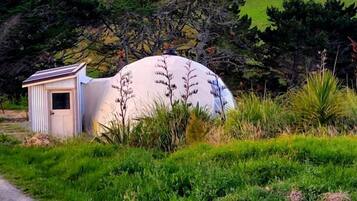 A dome-shaped structure with a small adjacent shed, surrounded by lush green fields and hills.