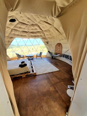 Una tienda de campaña con piso de madera, una cama, una mesa, sillas y vistas al paisaje.