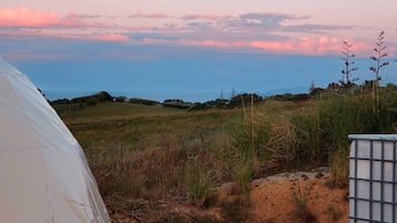 A tent in a grassy field with a view of the horizon.