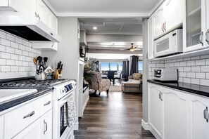 A kitchen with white cabinets, a stove, and a microwave. There is a dining area with a table and chairs. - Charming Cottage on Lake Erie for an Unforgettable Kingsville Getaway in Ontario (Kingsville)