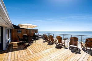 Eine Holzterrasse mit Sitzgelegenheiten im Freien, einem Grill und Blick auf den Ozean.