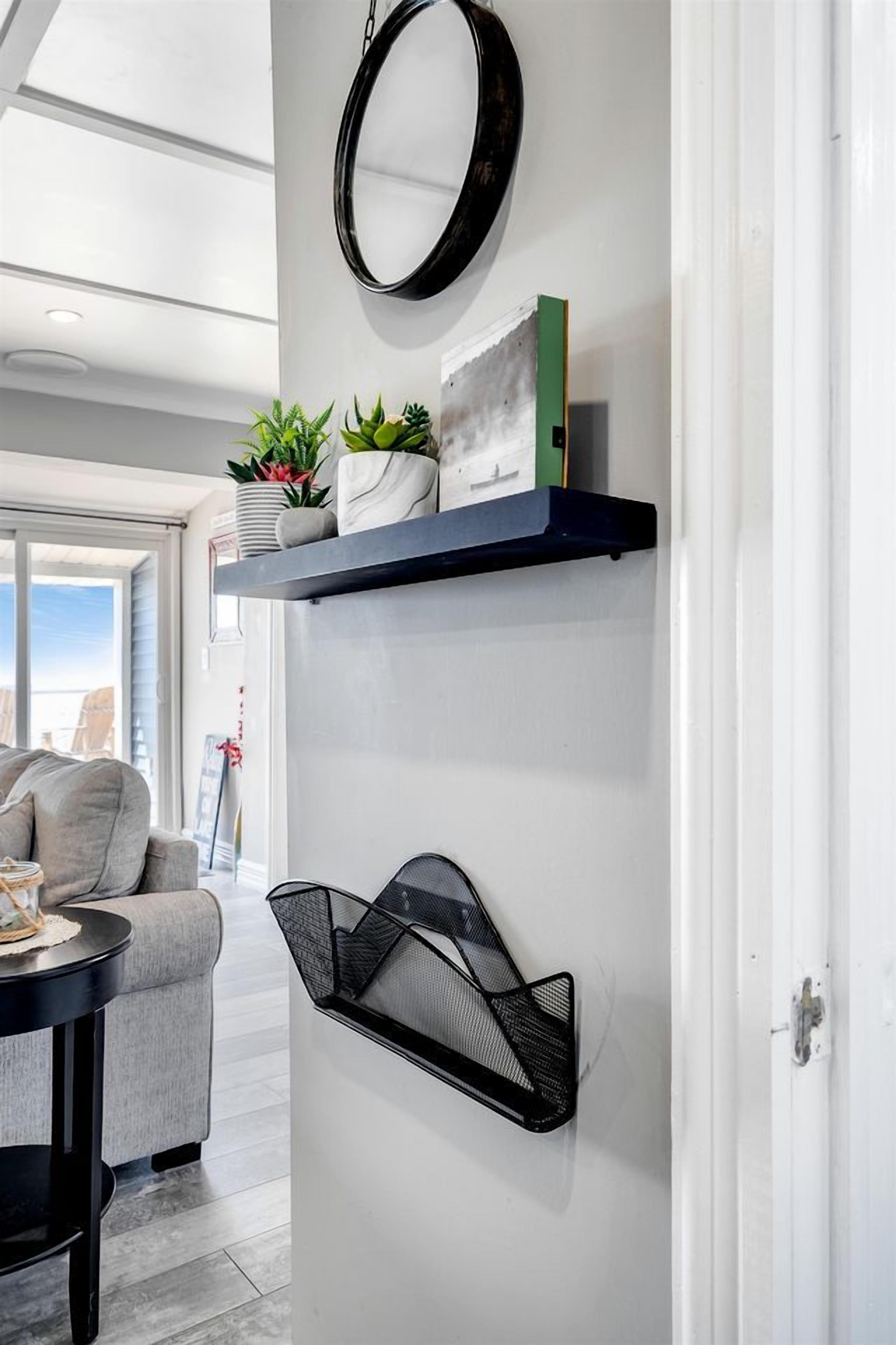 A modern interior with a sofa, a round mirror, and shelves with plants and books.