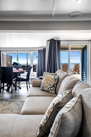 Un salon moderne comprenant un canapé, une table à manger et des chaises, avec vue sur l’océan grâce à de grandes fenêtres.