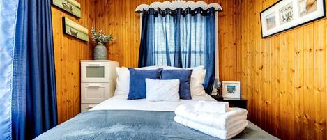 Une chambre avec un mur en bois, un lit avec une literie bleue, une table de chevet et une fenêtre avec des rideaux bleus.