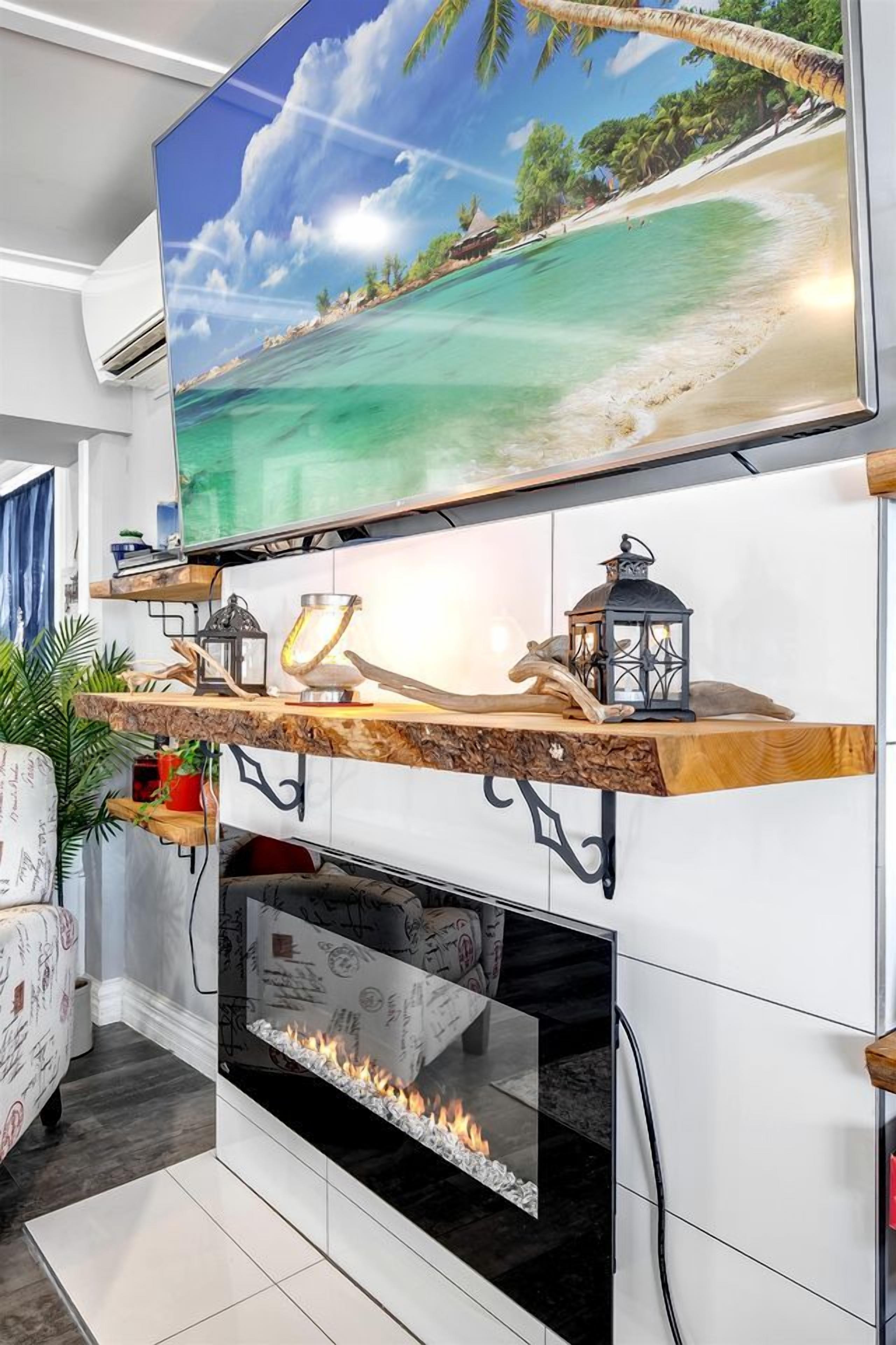 A modern living room with a flat-screen TV mounted above a fireplace, wooden shelves with decorative items, and a cozy seating area.