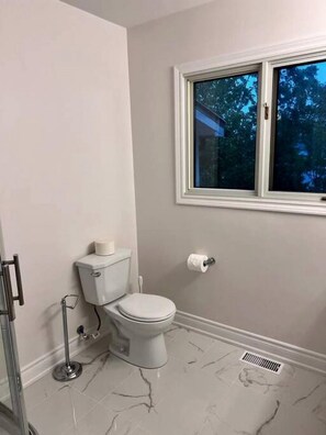 Une salle de bain équipée de toilettes, d’une barre d’appui, d’une fenêtre et d’un sol en marbre.