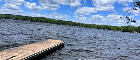 A wooden dock extending into a lake with a clear sky and a forested shoreline.