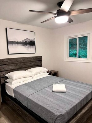 Une chambre à coucher avec un lit, un ventilateur de plafond, une fenêtre et un tableau encadré au mur.