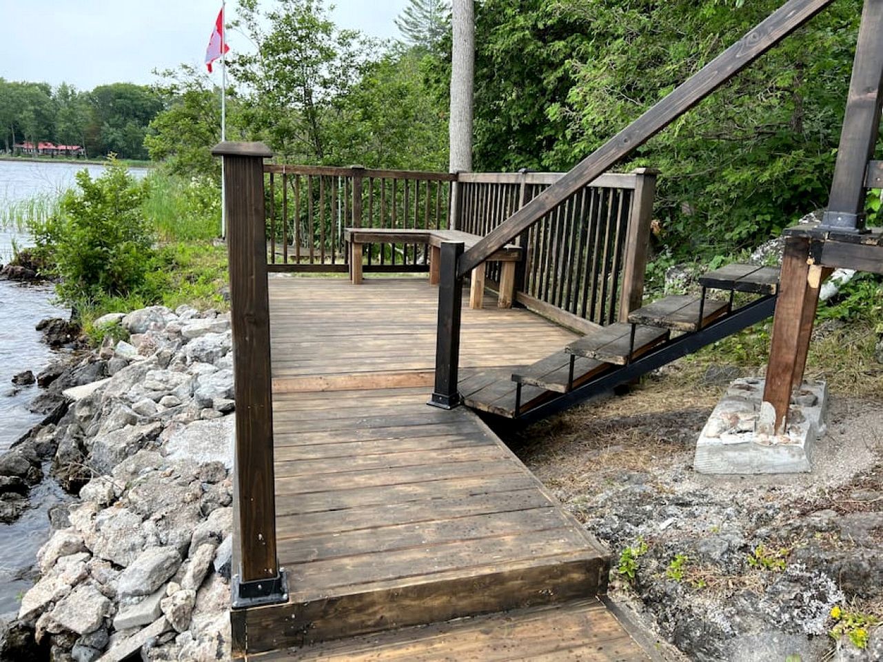 A wooden deck with a railing, leading to a bench area by a body of water.