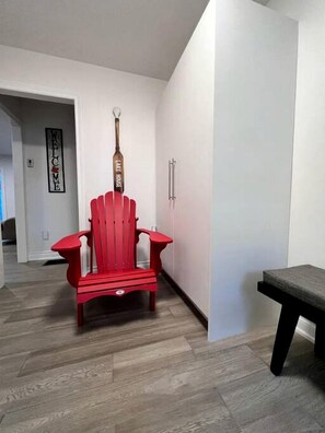 Ein roter Adirondack-Stuhl in einer Diele mit einem 'Welcome'-Schild und einem 'Lake House'-Schild an der Wand.