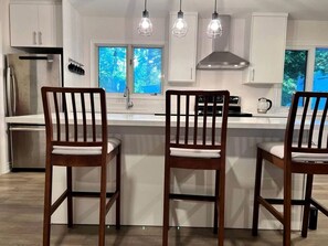 Una cocina moderna con armarios blancos, un refrigerador de acero inoxidable, un lavamanos doble y sillas de madera.