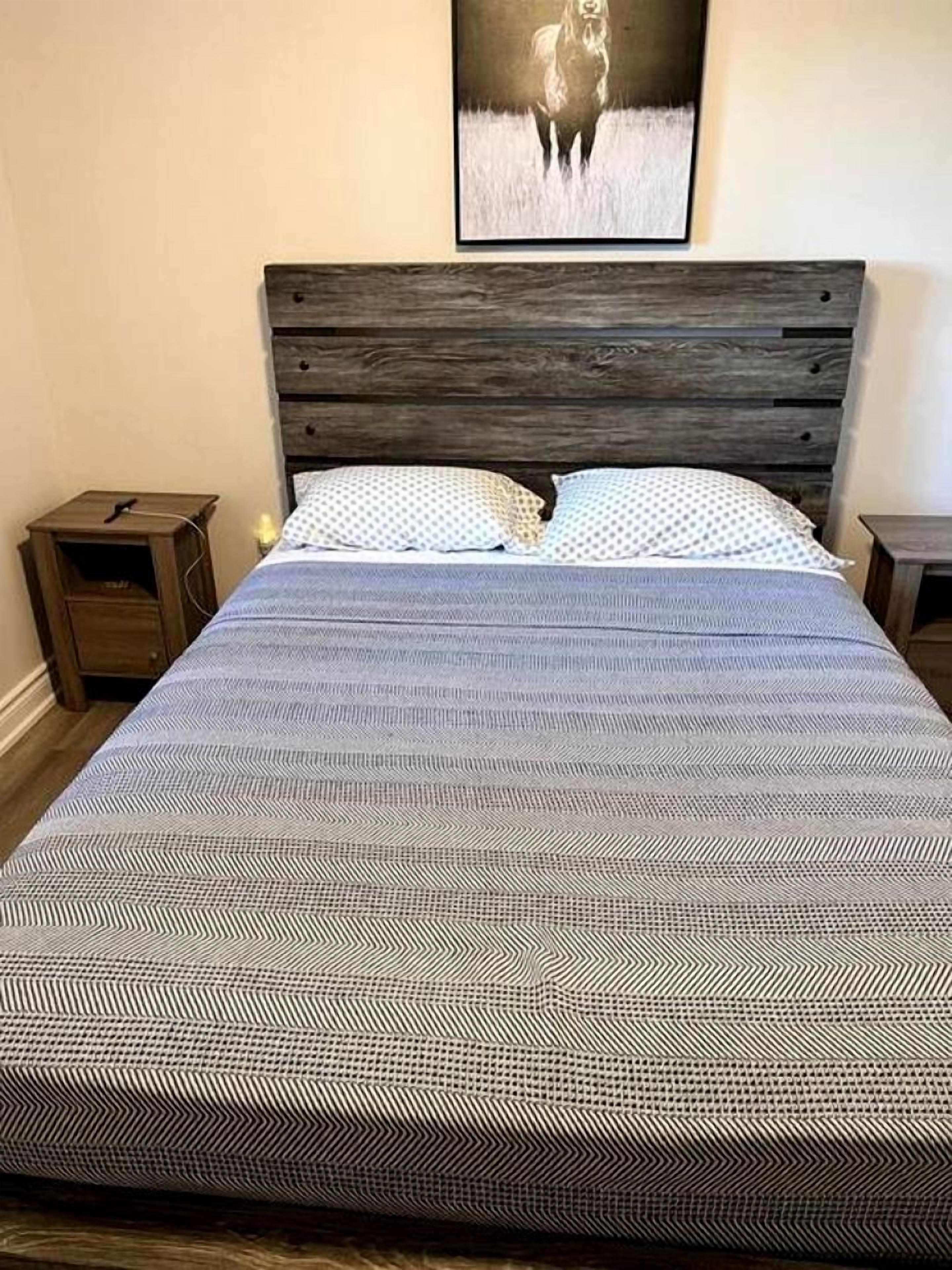 A bed with a patterned bedspread, wooden headboard, two bedside tables, and a framed picture on the wall.