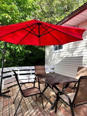 Une terrasse avec une table et des chaises, un parasol, et une maison blanche en arrière-plan.