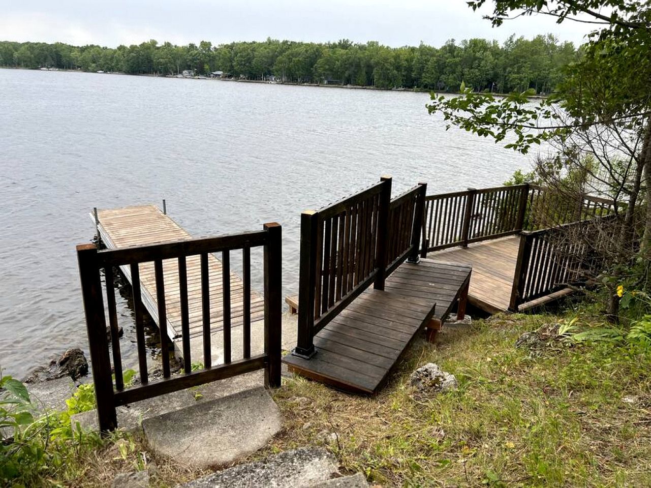A wooden dock extending into a lake with a wooden walkway and a metal railing.