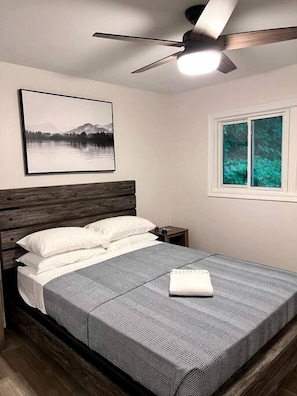 Ein Schlafzimmer mit Bett, Deckenventilator, Fenster und einem gerahmten Bild an der Wand.