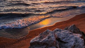 A beach with waves, a sunset, and rocks in the foreground. - Coast Rental with Hot-Tub and Equipped Deck in Ontario (Leamington)