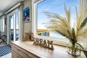 A room with a wooden desk, a 'DREAM' sign, a painting, and a view of the beach through a window. - Coast Rental with Hot-Tub and Equipped Deck in Ontario (Leamington)
