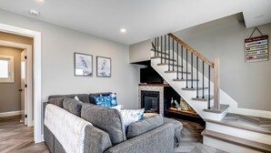 A modern living room with a grey sofa, a fireplace, and a staircase with wooden railings. - Coast Rental with Hot-Tub and Equipped Deck in Ontario (Leamington)