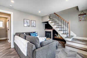 Uma sala de estar moderna com um sofá cinza, uma lareira e uma escada com guarda-corpos de madeira.