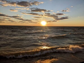 A sunset over the ocean with waves approaching the shore. - Coast Rental with Hot-Tub and Equipped Deck in Ontario (Leamington)