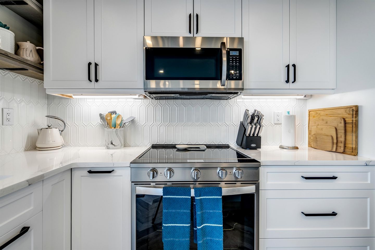 A kitchen with white cabinets, a stainless steel microwave, a gas stove, and a wooden cutting board.