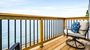 A wooden deck with a metal railing, a single chair with a cushion, and a view of the water. - Coast Rental with Hot-Tub and Equipped Deck in Ontario (Leamington)