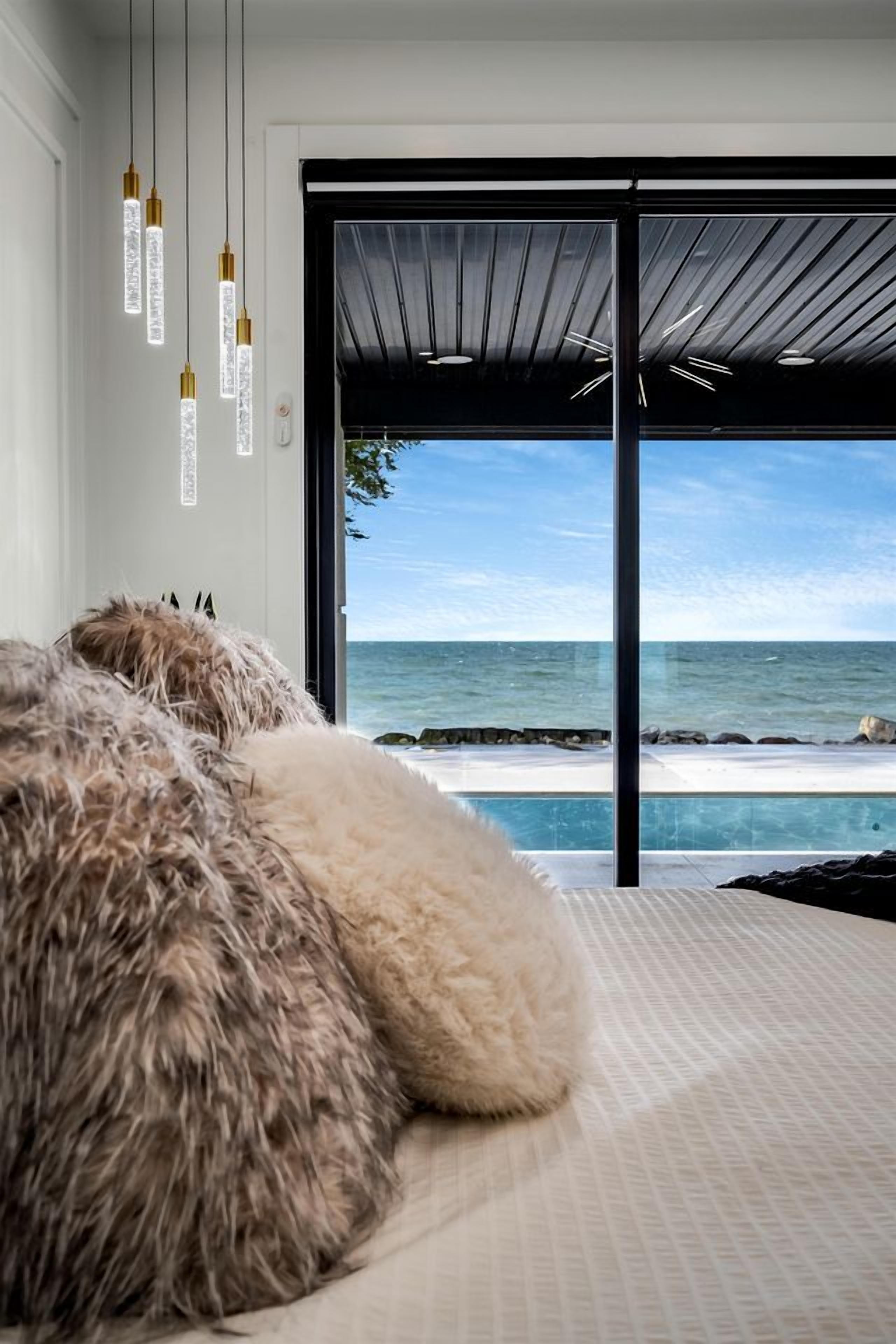A bedroom with a large bed, a view of the ocean, and hanging pendant lights.